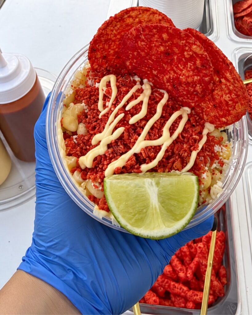 Elote en vaso topped with hot chips, crema and lime